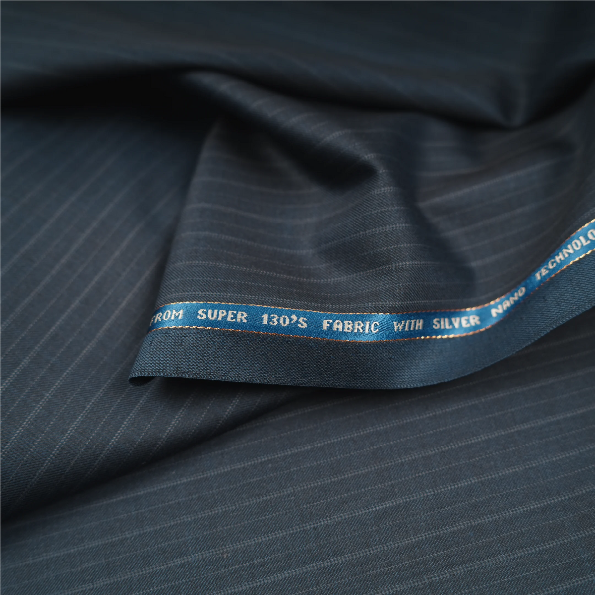 Close-up of Raymond Lexican Merino Wool 130 teal blue fabric with pinstripes and branded selvedge