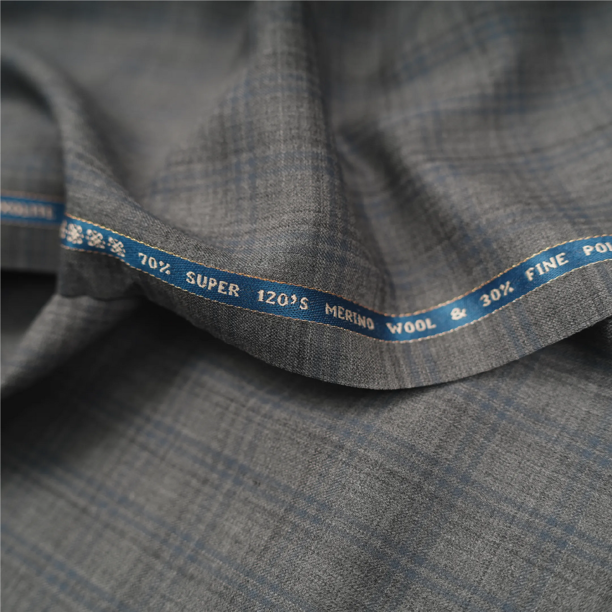 Close-up of Raymond Luxolite Merino Wool 120 light grey fabric with blue checks and branded selvedge