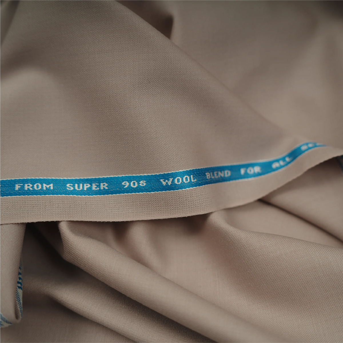 Close-up of Raymond Exotic Techno Stretch Super 90's beige wool blend fabric with branded selvedge