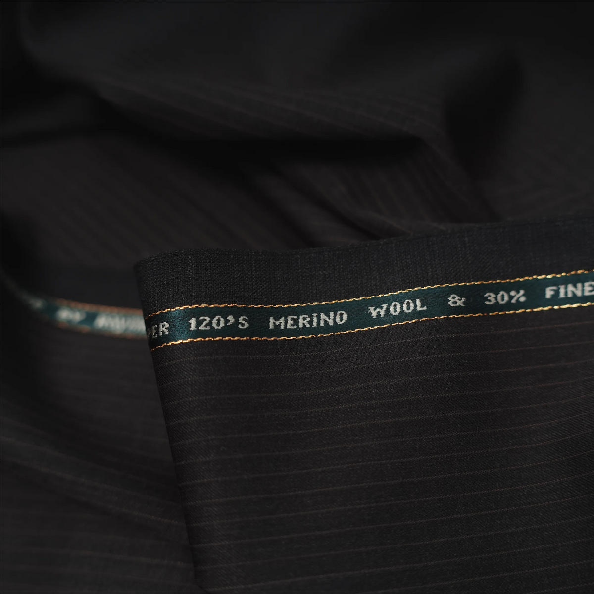 Close-up of Raymond Luxolite Merino Wool 120 dark brown fabric with pinstripes and branded selvedge