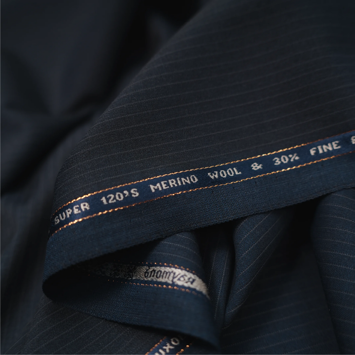 Close-up of Raymond Luxolite Merino Wool 120 dark navy fabric with pinstripes and branded selvedge